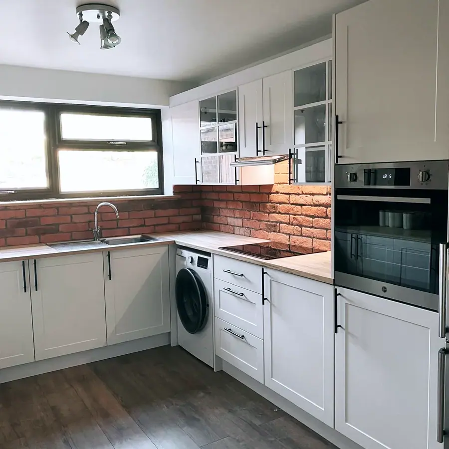 White shaker kitchen with black bar handles and a brick splashback